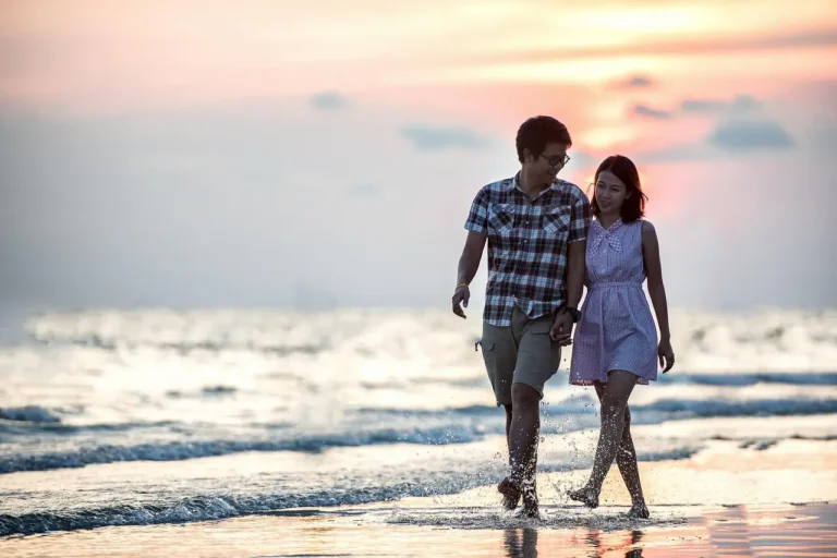 Un couple marchant les pieds dans l'eau au bord de la plage pour présenter un article de blog sur la manière de séduire un homme poisson