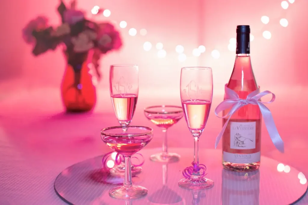 Que faire le 31 décembre en couple - Photo inspirante avec une bouteille, deux flutes et deux verres à cocktail sur un fond rose